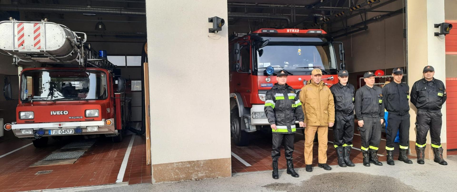 Zdjęcie przedstawia zastępcę świętokrzyskiego komendanta wojewódzkiego PSP w Kielcach st. bryg. Grzegorza Rajcę, podczas wizytacji Posterunku Mieszanego w Sędziszowie. Obok świętokrzyskiego komendanta wojewódzkiego PSP ustawieni w szeregu strażacy pełniący tego dnia służbę w umundurowaniu specjalnym oraz komendant powiatowy PSP w Jędrzejowie mł. bryg. Mariusz Stolarczyk. Za ich plecami ustawione dwa samochody ratowniczo-gaśnicze w garażu.