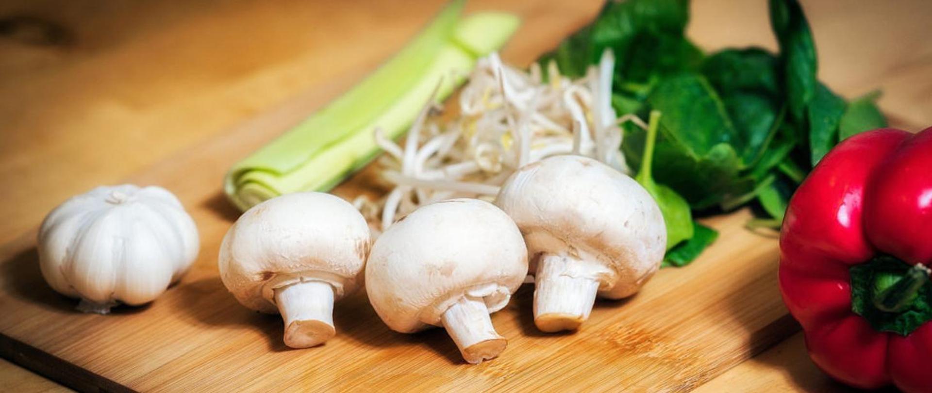 na stole kuchennym, leżą pieczarki, czosnek, por i papryka 