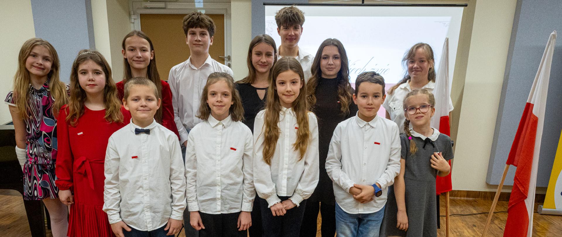 Grupa dzieci z nauczycielką stoją obok dwóch flag państwowych.