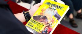 一位书展嘉宾手里拿着波兰科幻大师拉法乌·科西克的小说《赛博朋克2077：无人幸存》中文版。背景中可以看到更多这本书的中文版。