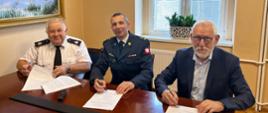 Zdjęcie przedstawia trzech mężczyzn podpisujących dokumenty. Na zdjęciu znajduje się Komendant Powiatowy PSP w Brzegu, Burmistrz Grodkowa i Prezes OSP Wierzbnik.