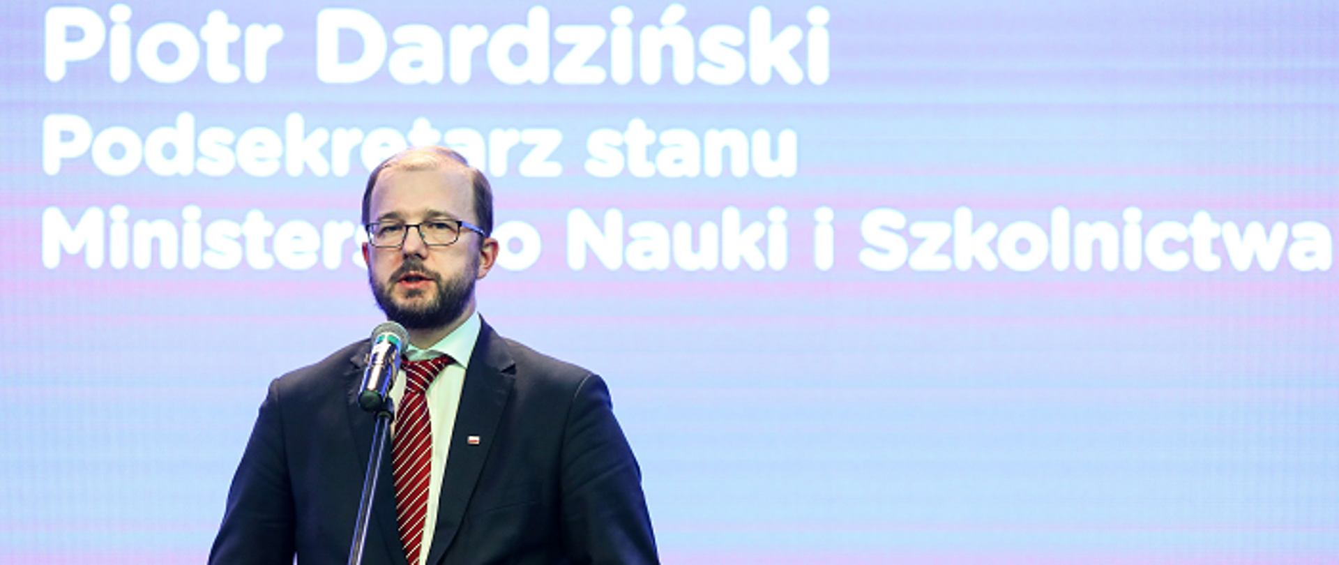 Minister Piotr Dardziński na tle jasnoniebieskiej ściany