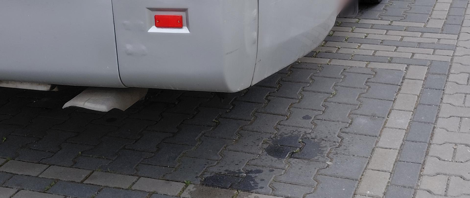 Na tylnej części autobusu widać ślady uszkodzeń karoserii oraz ciemne plamy cieczy na kostce brukowej pod pojazdem, sugerujące możliwy wyciek.
