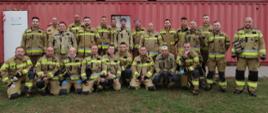 Grupowe zdjęcie strażaków (25 osób) w ubraniach bojowych na tle kontenera rozgorzeniowego