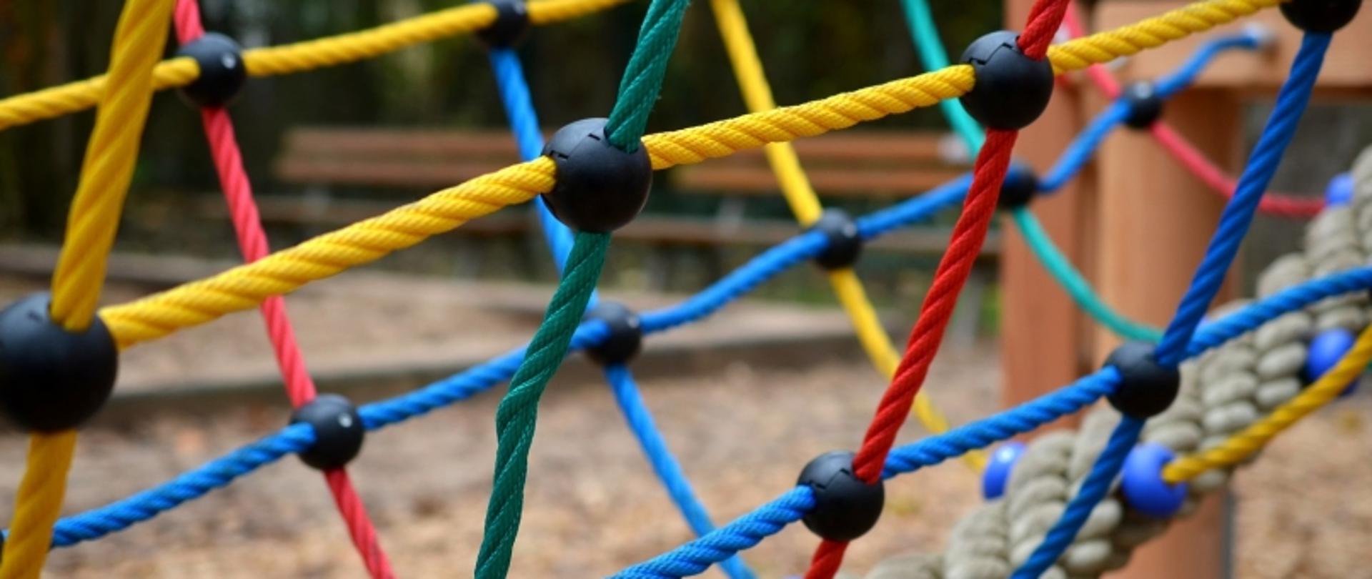 Kolorowa siatka wspinaczkowa z lin na placu zabaw, z czarnymi węzłami i rozmytym tłem.