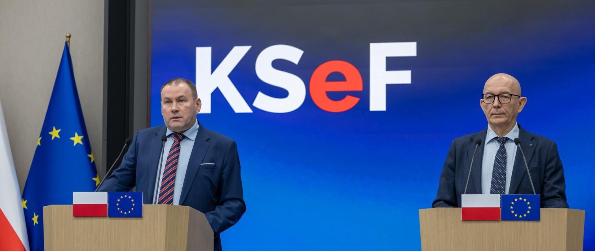 Zbigniew Stawicki, Podsekretarz Stanu w Ministerstwie Finansów, Zastępca Szefa Krajowej Administracji Skarbowej oraz Roman Łożyński, dyrektor Centrum Informatyki Resortu Finansów przy mównicach z flagami Polski i Unii Europejskiej na tle ekranu z logo KSeF