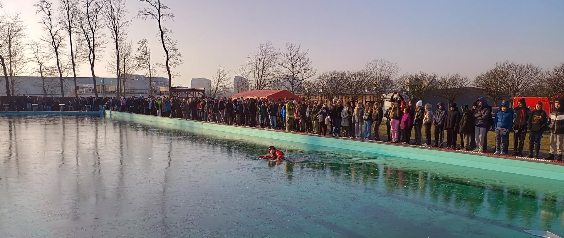 Jeden ze strażaków wszedł do basenu skutego cienkim lodem i przygotowuje się do pokazu.