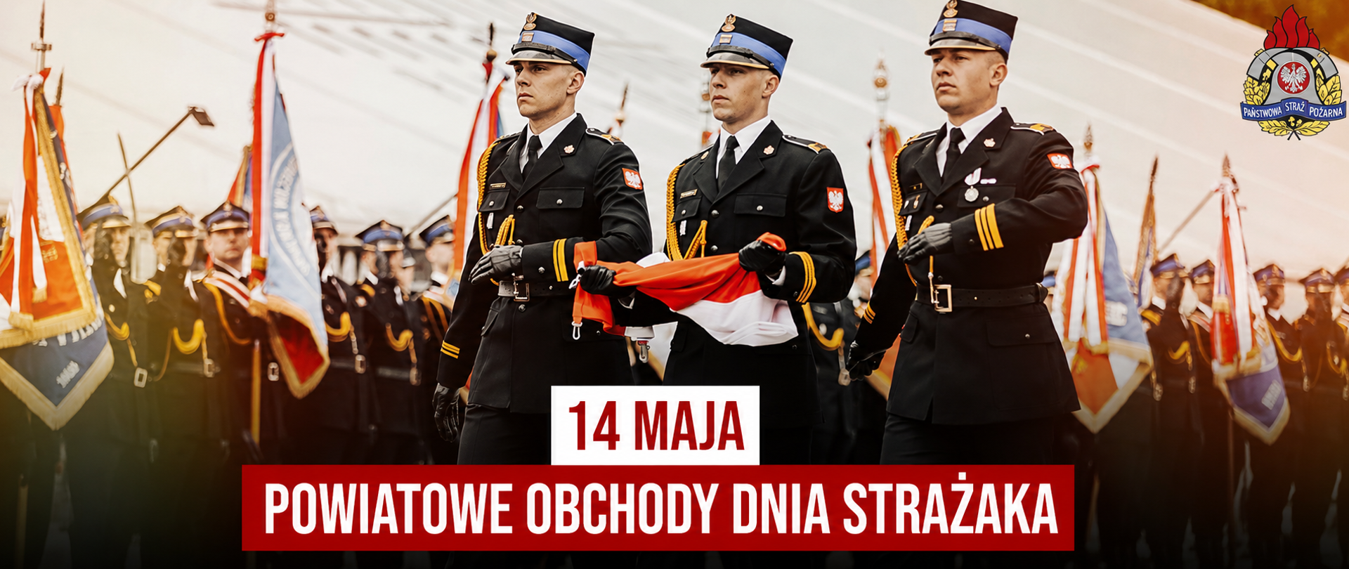 Zdjęcie przedstawiające strażaków niosących flagę państwową. W tle poczty sztandarowe PSP. 