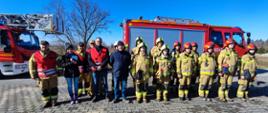 Na zdjęciu strażacy oraz pracownicy obiektu stoją w szeregu w tle widoczne są samochody strażackie