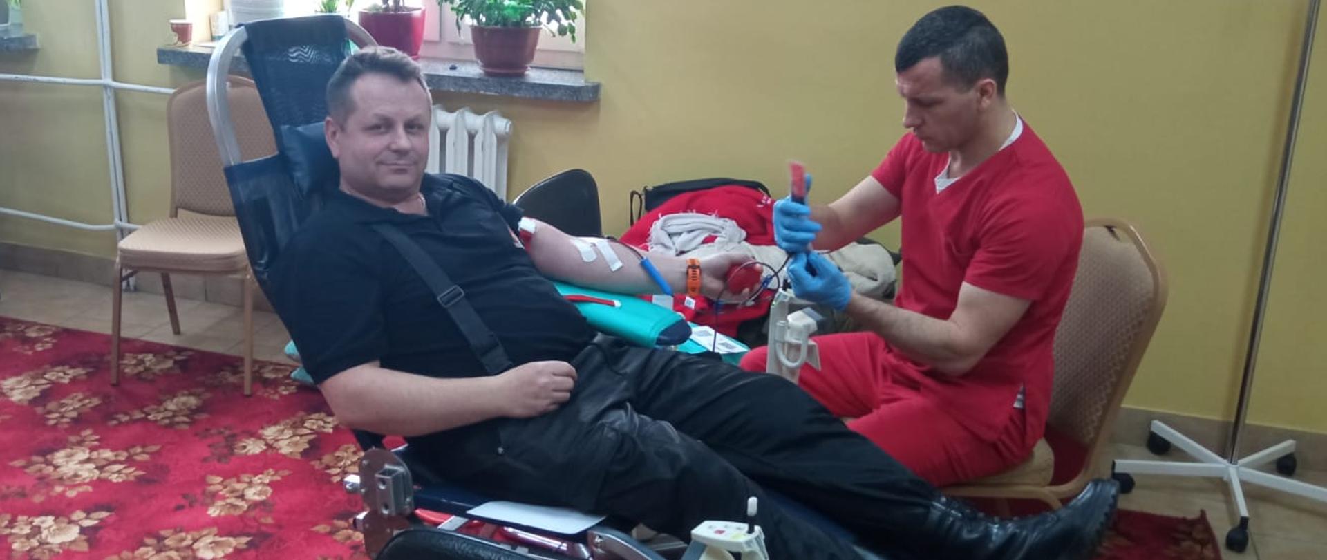 Zdjęcie przedstawia kolejnego ze strażaków Komendy Powiatowej Państwowej Straży Pożarnej w Gołdapi, który oddaje krew w ramach akcji wpisującej się w Ogólnopolską zbiórkę krwi z okazji Narodowego Dnia Pamięci Żołnierzy Wyklętych – „spoKREWnieni służbą”