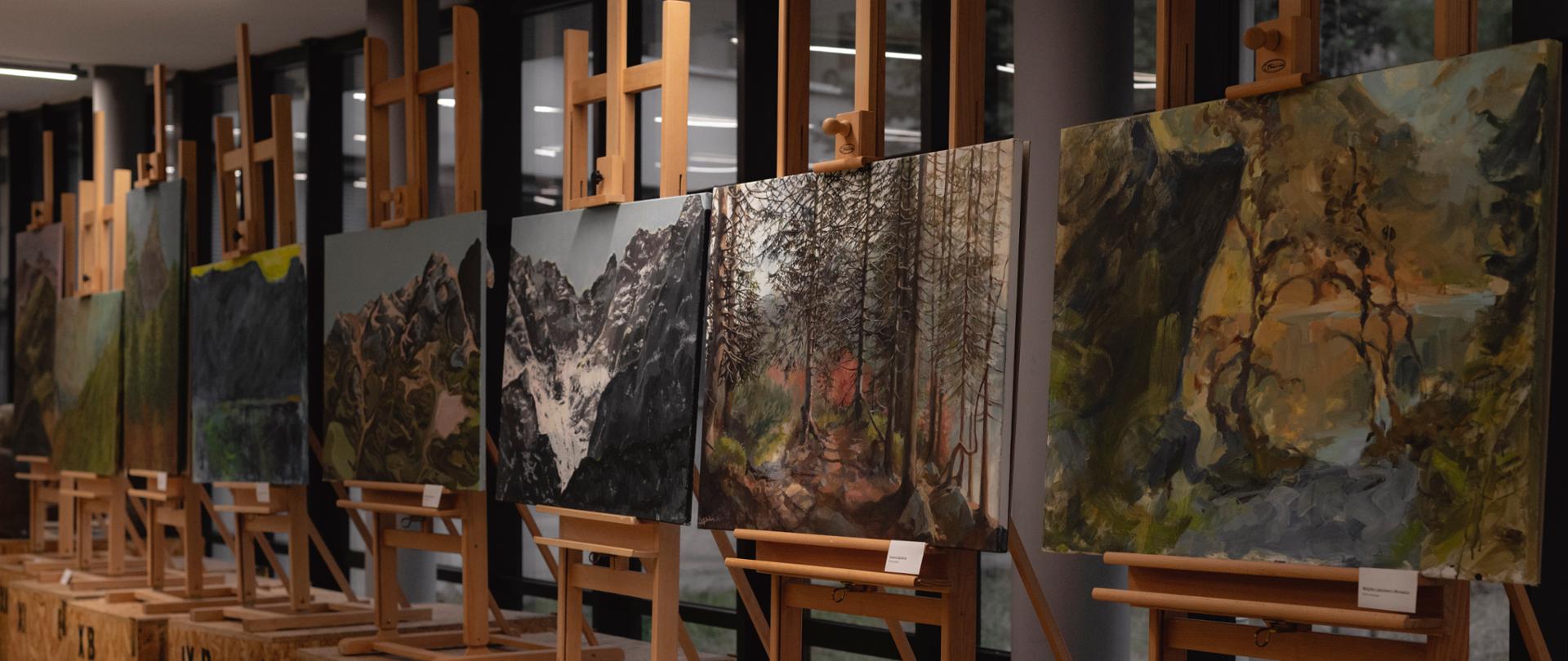 Na zdjęciu prace malarskie - pejzaż górski w Morskim Oku. Obrazy eksponowane są na drewnianych sztalugach.