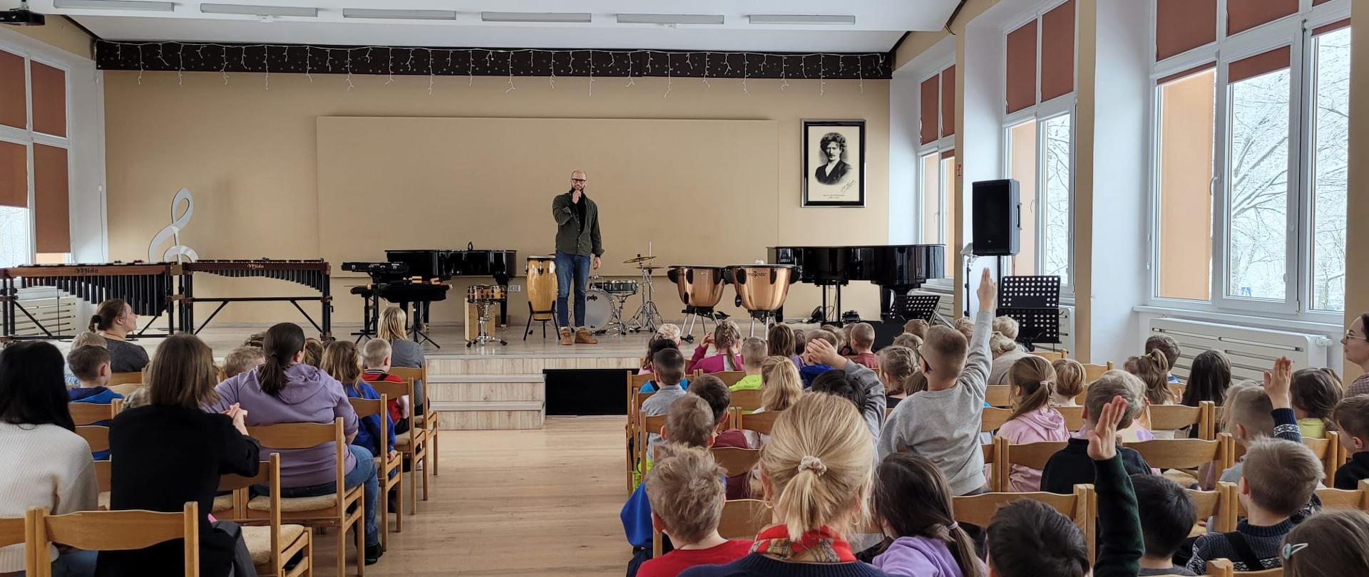 na scenie nauczyciel omawiający instrumenty perkusyjne, na widowni grupa przedszkolaków
