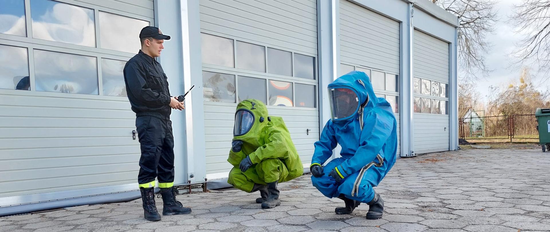 Na zdjęciu widnieją strażacy w trakcie kursu z zakresu ratownictwa chemiczno ekologicznego. Zajęcia odbywają się na zewnątrz pomieszczenia, jest dzień i słonecznie. 