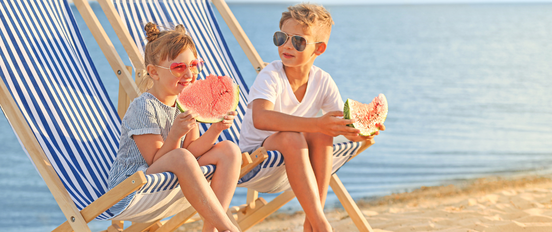 Mały chłopiec i mała dziewczynka siedzący na leżakach na plaży i jedzący arbuza.