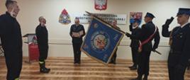 Moment uroczystego ślubowania. Nowi funkcjonariusze trzymają prawą rękę w górze, wygłaszając słowa roty, którą odczytuje komendant powiatowy. Funkcjonariusze znajdujący się w poczcie sztandarowym zachowują postawę zgodną z ceremoniałem pożarniczym. 