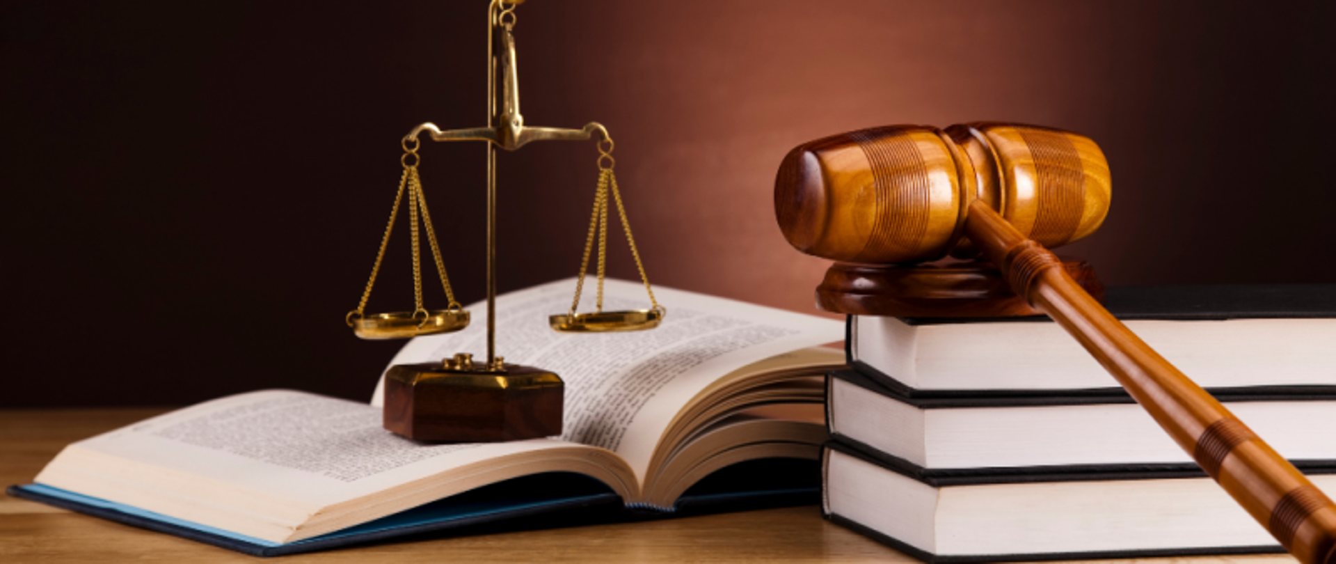 Blat biurka. Na nim leżą książki, młotek sędziowski na podstawce i ozdobna waga.