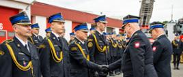 Fotografia przedstawia moment wręczania awansów podczas oficjalnej uroczystości Dnia Strażaka, odbywającej się na placu przed budynkiem remizy.