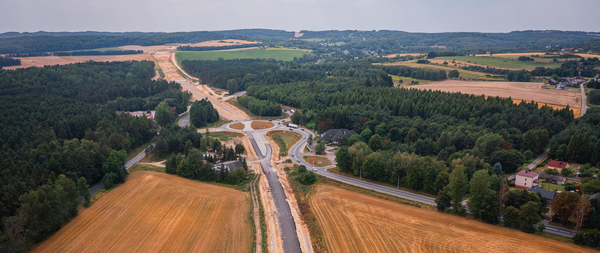 Styk obejścia Kroczyc z odcinkiem obwodnicy Poręby i Zawiercia (Kromołów - Żerkowice). Przy trasie znajdują się pola uprawne oraz tereny leśne. Skomunikowane z drogą są stacja paliw (lewa strona fotografii) oraz lokalny punkt gastronomiczny (po prawej stronie). Kierunek zdjęcia: Zawiercie.