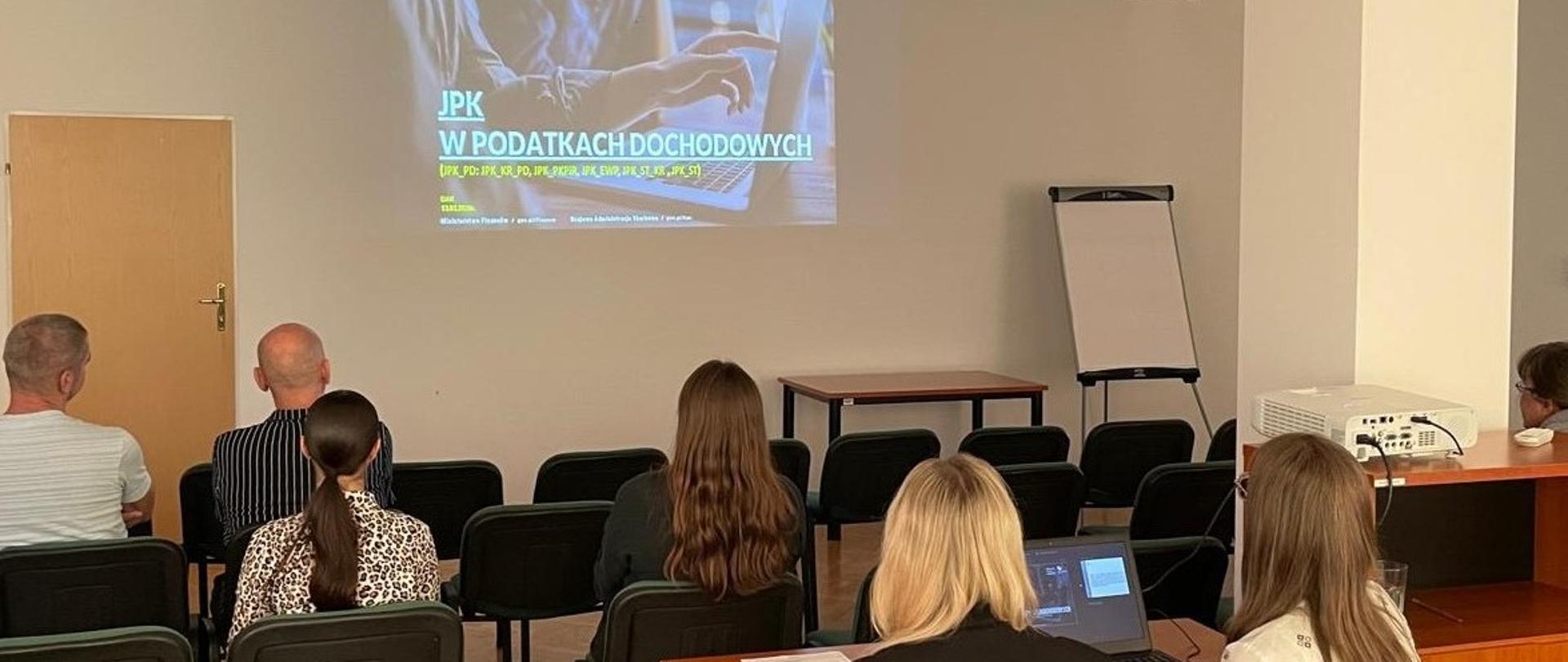 Uczestnicy siedzą w sali. Na ekranie wyświetlana jest prezentacja.