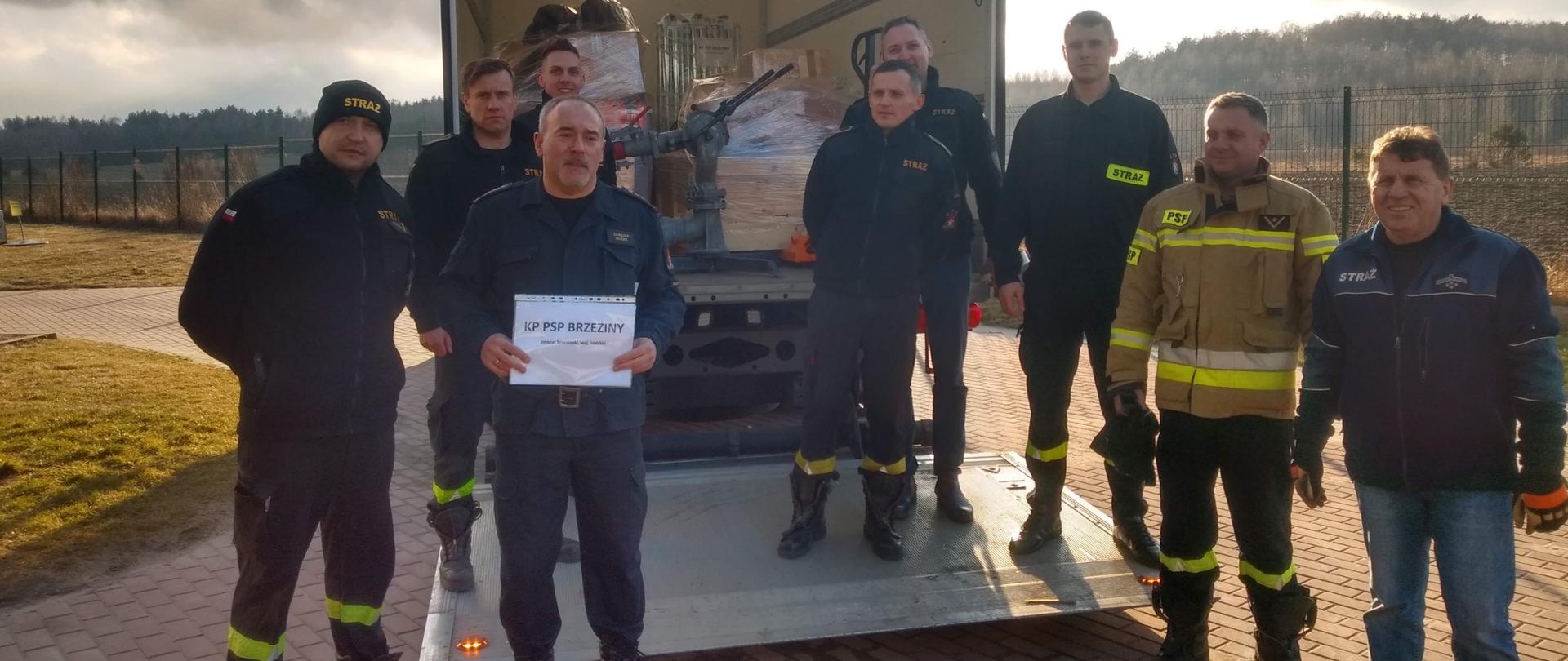 Załadowany sprzętem strażackim samochód typu bus . Przed samochodem strażacy z Komendy Powiatowej PSP w Brzezinach