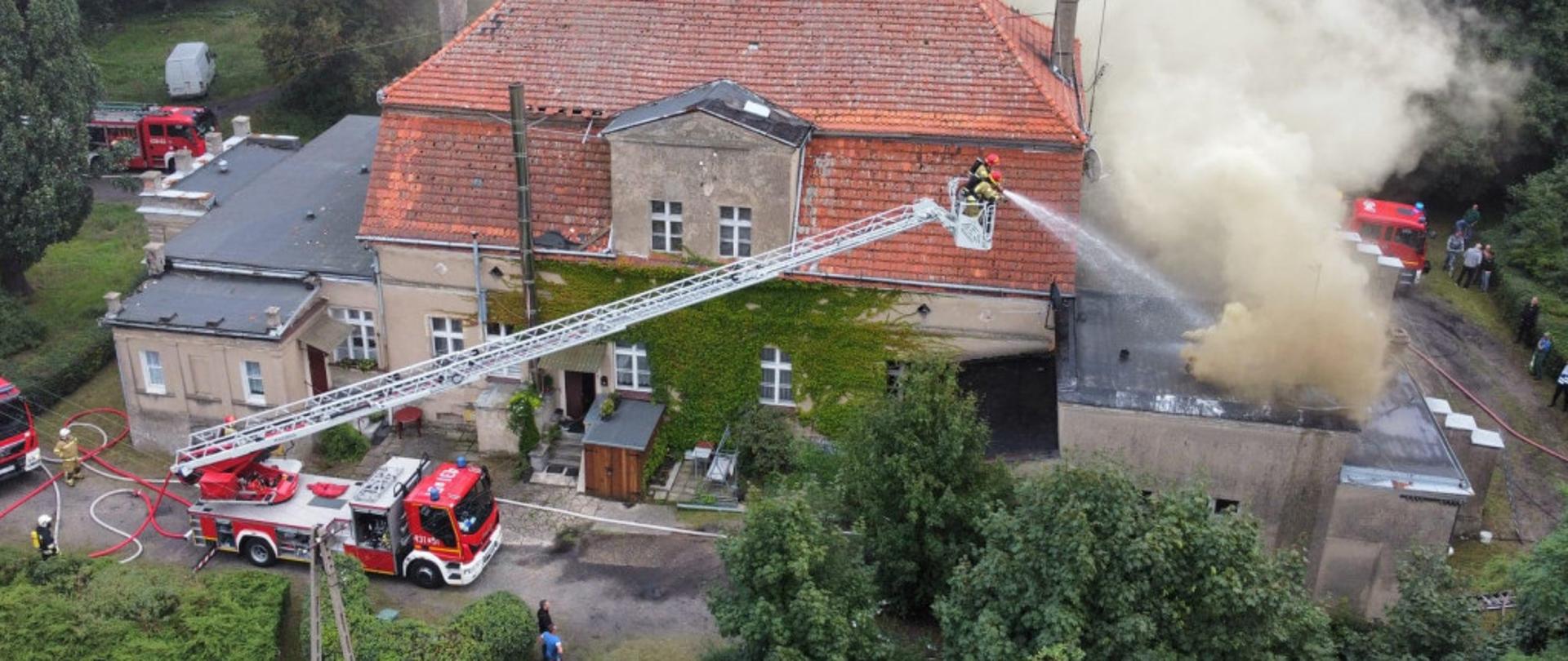 Widok z lotu ptaka palącego się pałacu oraz prowadzenie działań straży z drabiny mechanicznej.