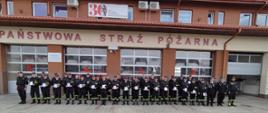 Na zdjęciu widoczna grupa druchów OSP z terenu powiatu strzyżowskiego stoją na zbiórce, w dłoniach rzymają zaświadczenia o ukończeniu kursu. Obok stoją funkcjonariusze KP PSP w Strzyżowie. W tle budynek komendy.
