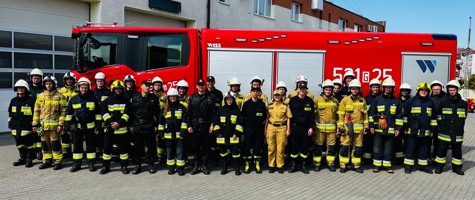 Zdjęcie przedstawia uczestników kursu podstawowego na tle ciężkiego samochodu pożarniczego