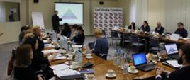 Zdjęcie przedstawia widok sali i uczestników spotkania. Są to uczestnicy spotkania – doradcy ds. etyki. W tle widać ekran, przy którym stoi prowadzący warsztaty dla doradców Jacek Bielawa z Wyższego Urzędu Górniczego w Katowicach, który objaśnia slajdy wyświetlanej prezentacji. Na prawo od ekranu stoi roll-up z napisem Szef Służby Cywilnej.