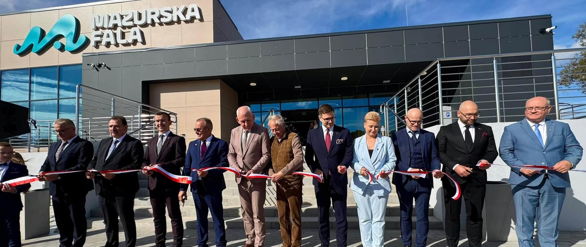 Uroczystość otwarcia pływalni „Mazurska Fala” w Działdowie, z grupą osób przed budynkiem i wstęgą.