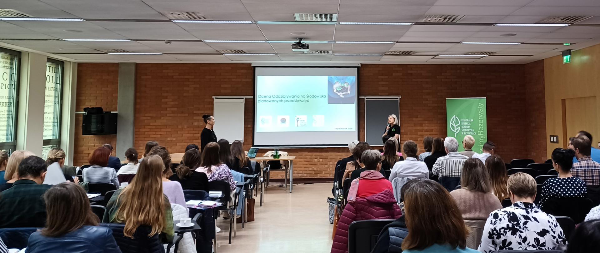 Sala wykładowa z prelegentami, uczestnikami i rzutnikiem z prezentacją