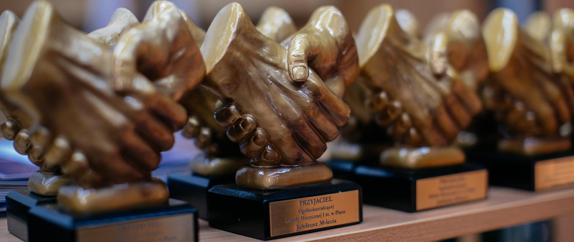 Zdjęcie statuetek przyjaciela szkoły w formie uścisku dłoni na rozmazanym tle.