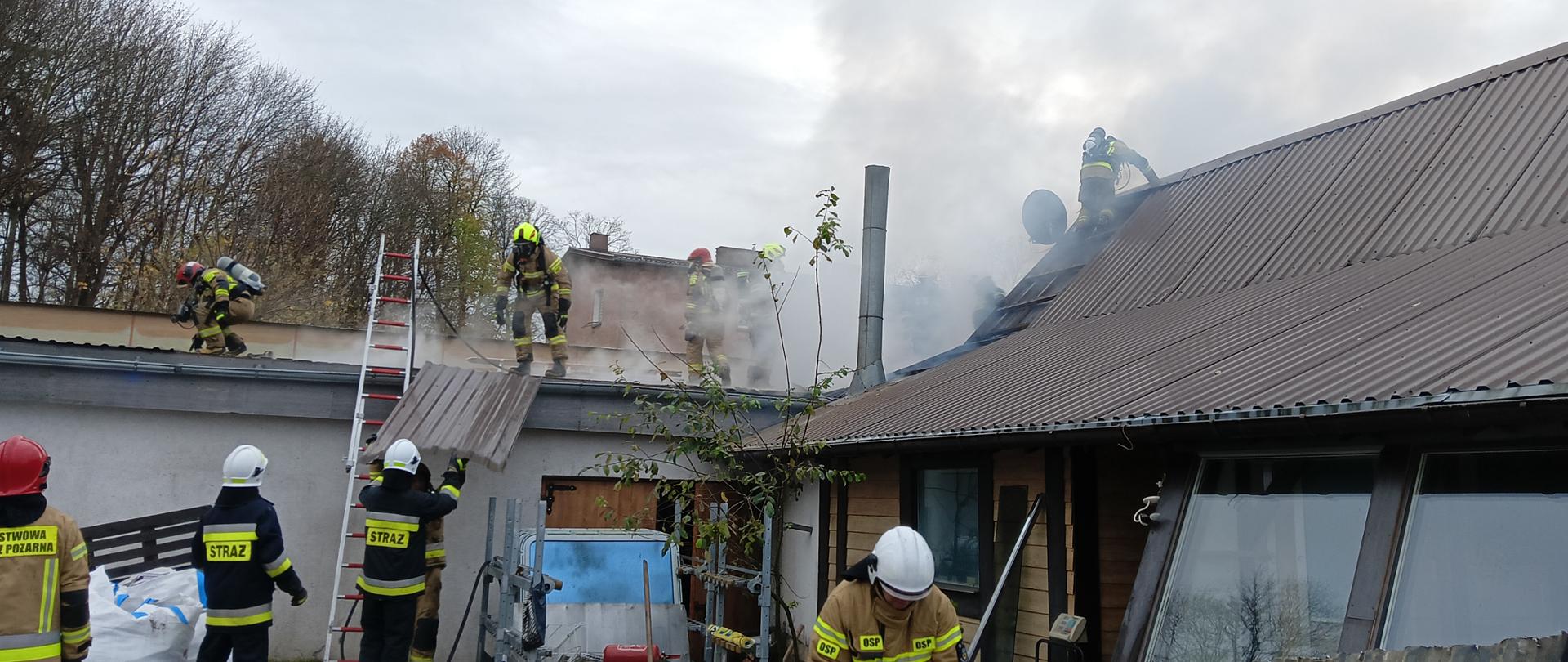 Strażacy podczas gaszenia pożaru konstrukcji dachu sklepu oraz przyległego budynku kotłowni. ratownicy rozbierają cześć pokrycia dachu.