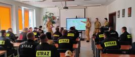 Zdjęcie przedstawia uczestników szkolenia kierowców-konserwatorów sprzętu ratowniczego OSP oraz komendanta powiatowego PSP i członków komisji egzaminacyjnej w sali szkoleniowej komendy.