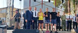 Zdjęcie przedstawia osoby na scenie, które zdobyły trzy pierwsze miejsca w klasyfikacji państwowa straż pożarna oraz osoby wręczające puchary. 