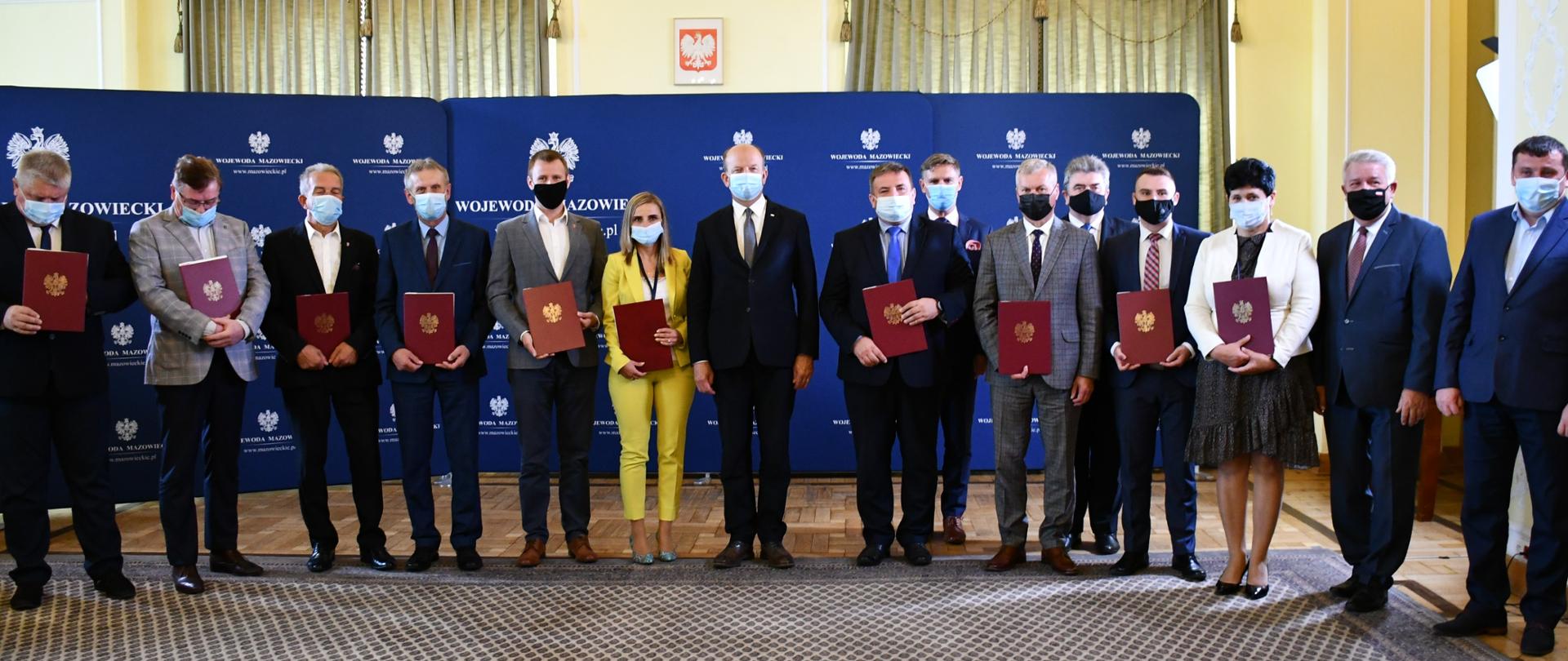 Na zdjęciu widoczne są osoby, które trzymają w rękach umowy