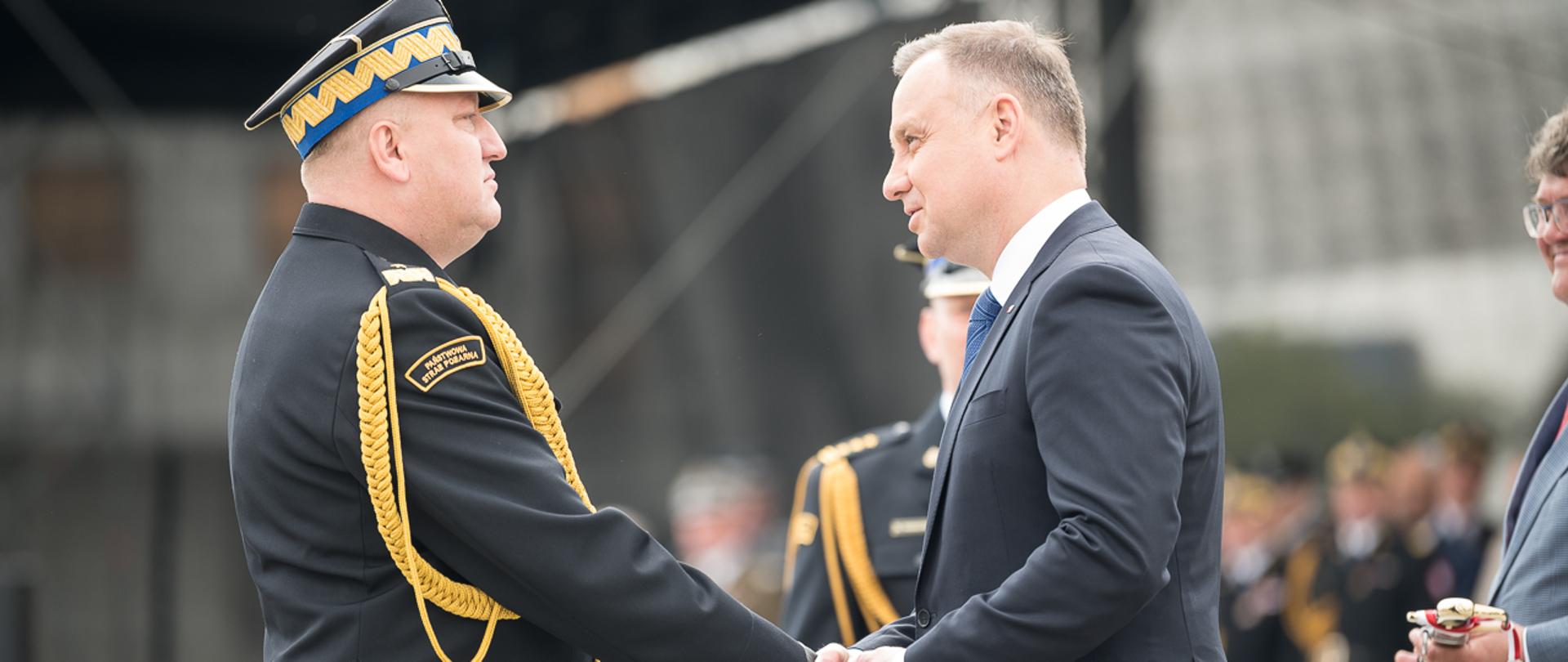 na zdjęciu strażak nadbrygadier Grzegorz Janowski oraz prezydent RP Andrzej Duda, stoją na przeciwko siebie i ściskają prawe dłonie