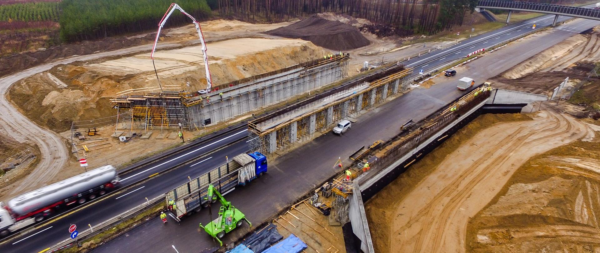 Trwa budowa podpór przejścia górnego dla zwierząt. Samochody poruszają się jedną jezdnią czynną dla ruchu.