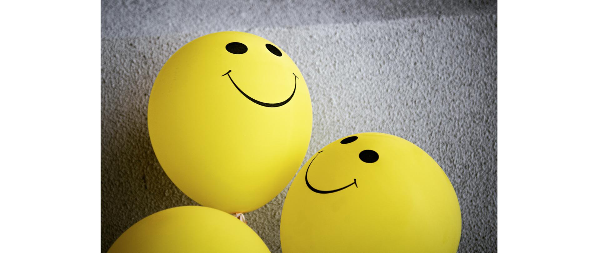 żółte balony z czarnymi oczkami i uśmiechem leżące na dywanie imitujące emotikony