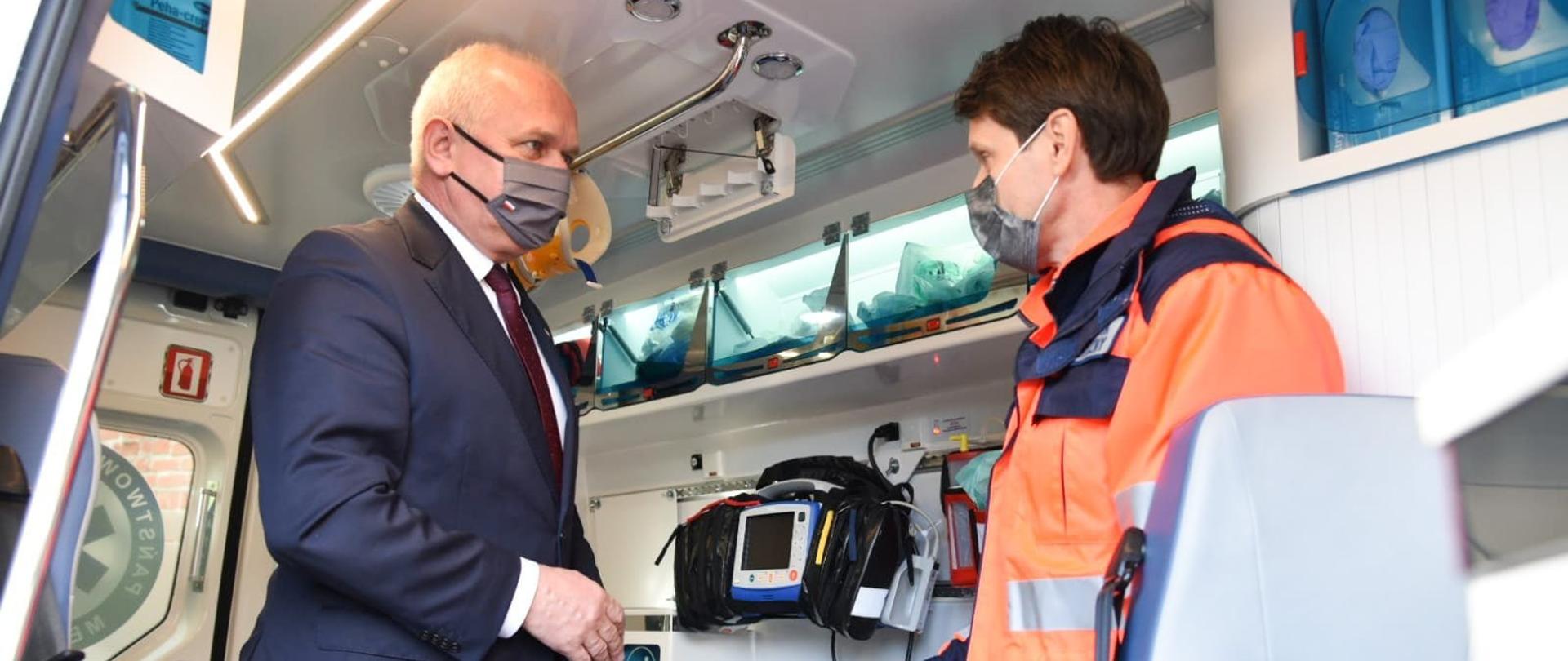 Wojewoda z maseczką na twarzy rozmawia z ratownikiem medycznym we wnętrzu karetki