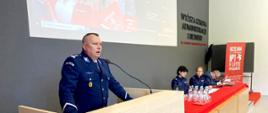 Policjant stoi przed mównicą i przemawia obok za stołem siedzą Policjantki oraz przedstawiciel uczelni.