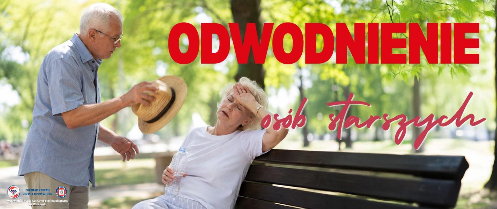 Dwie starsze osoby w w parku przy ławeczce. Starszy pan wachluje panią siedzącą na ławeczce kapeluszem słomkowym. Pani jest odwodniona i zasłabła, Pani trzyma w ręce butelkę wody . Wokoło panuje upał