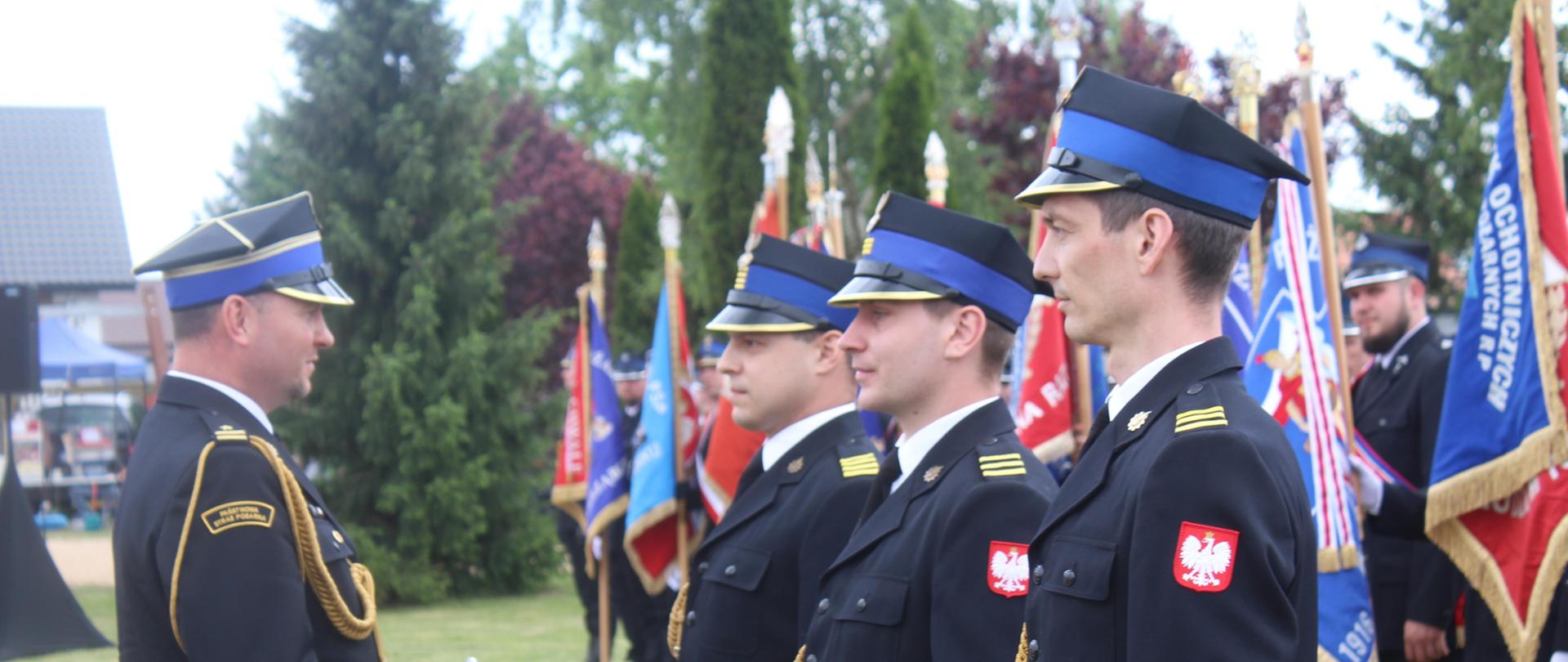 Naczelnik Wydziału Organizacji i Nadzoru – reprezentujący Wielkopolskiego Komendanta Wojewódzkiego PSP wręcza akty wyróżnionym, w tle poczty sztandarowe