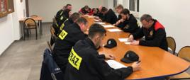 Na zdjęciu druhowie z Ochotniczych Straży Pożarnych z powiatu gorlickiego ubrani w czarne ubrania koszarowe w sali konferencyjnej w Komendzie Powiatowej Państwowej Straży Pożarnej podczas recertyfikacji uprawnień z zakresu kwalifikowanej pierwszej pomocy rozwiązujący test.