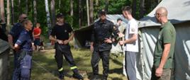 Zdjęcie przedstawia funkcjonariuszy Komendy Powiatowej Państwowej Straży Pożarnej w Krośnie Odrzańskim, funkcjonariuszy Komendy Powiatowej Policji w Krośnie Odrzańskim, przedstawiciela Nadleśnictwa Bytnica, Komendanta Obozu Harcerskiego „Struga” oraz harcerzy podczas kontroli w ramach akcji „Bezpieczne Wakacje 2021”. Zdjęcie wykonane zostało na tle namiotów w Obozie Harcerskim „Struga”.