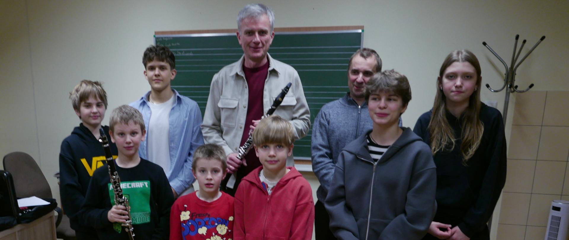 Na fotografii widzimy chłopców i dziewczyny z klasy klarnetu, niektórzy z nich trzymają w dłoniach instrumenty. Widzimy rownież prowadzącego warsztaty klarnetowe nauczyciela , oraz pana który uczy klarnetu wszystkich ze zdjęcia.