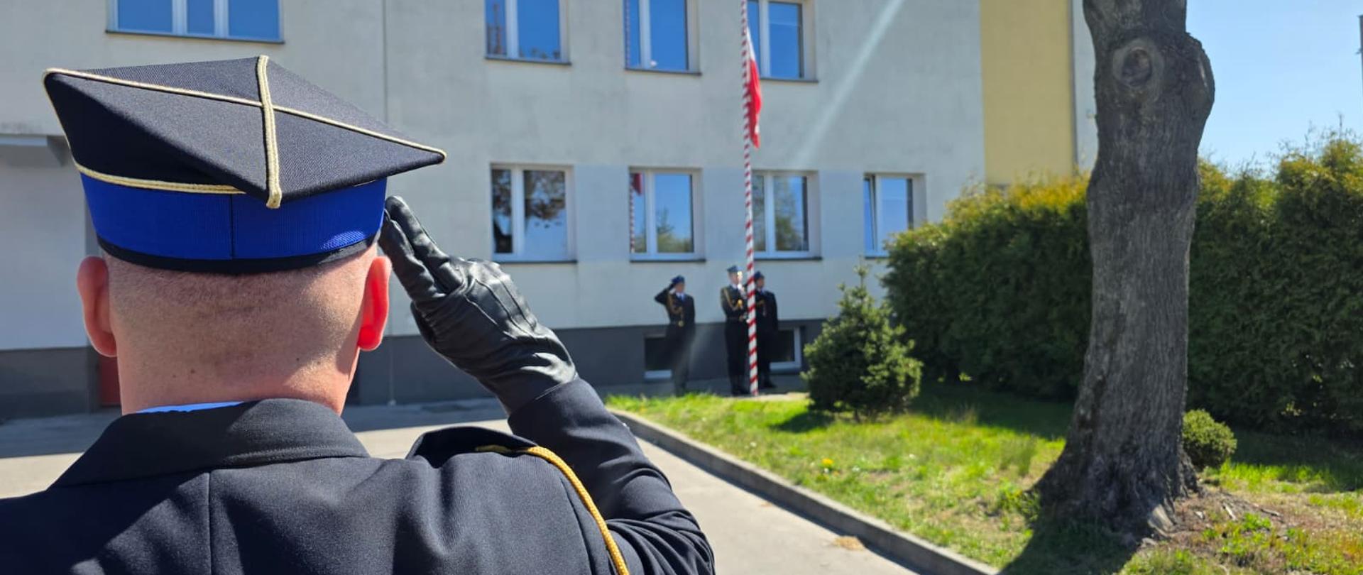 Funkcjonariusz Państwowej Straży Pożarnej w Jaworznie oddaje salut podczas uroczystego podniesienia flagi Rzeczypospolitej Polskiej na placu przed budynkiem komendy.