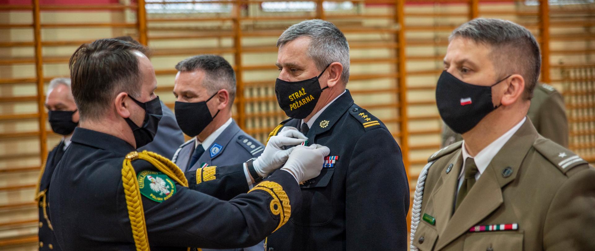 Komendant Morskiego Oddziału Straży Granicznej przypina medal do munduru pomorskiego komendanta wojewódzkiego Państwowej Straży Pożarnej. 