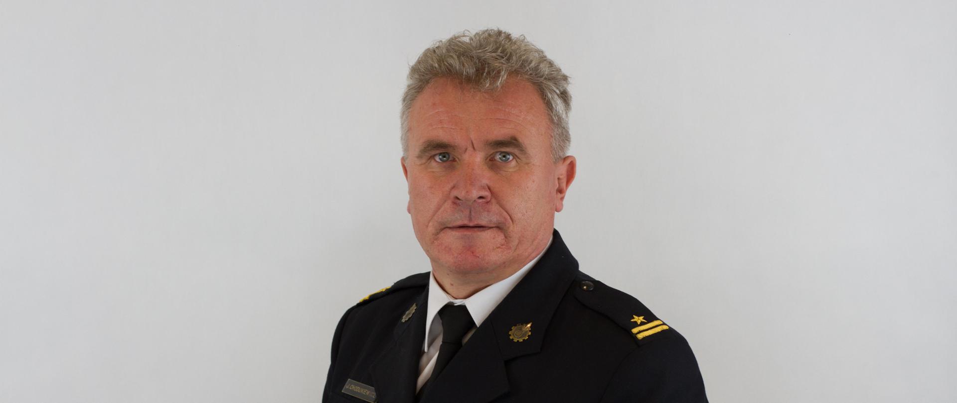 Na zdjęciu znajduje się Komendant Powiatowy Państwowej Straży Pożarnej w Pruszczu Gdańskim mł. bryg. Jan Chodukiewicz na jednolitym szarym tle.