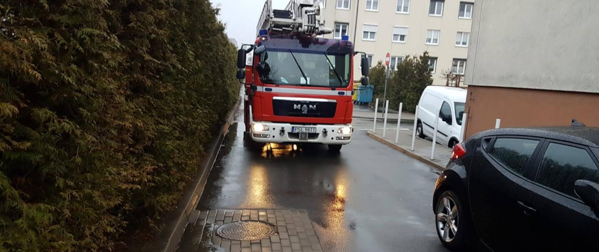 Samochód strażacki wjeżdża na osiedle przed nim stoi samochód