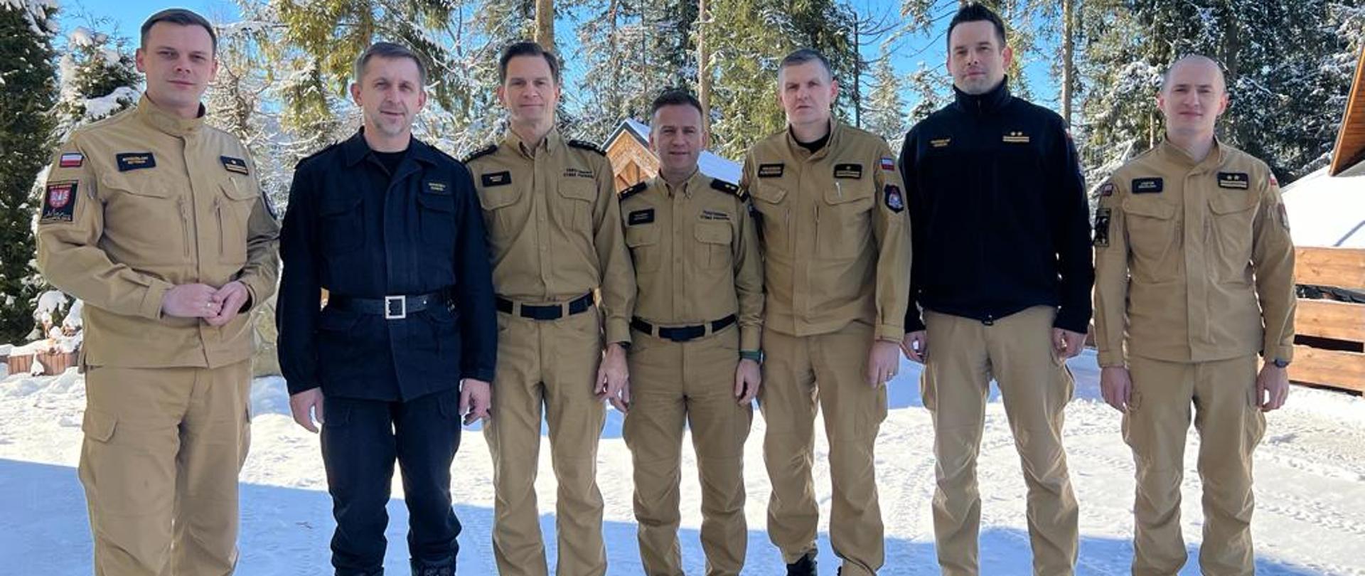 strażacy stoją w ubraniu służbowym na zewnątrz w tle drzewa